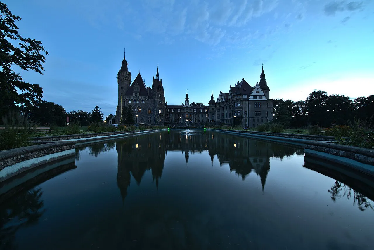 Moszna Castle reflected in water at blue hour.