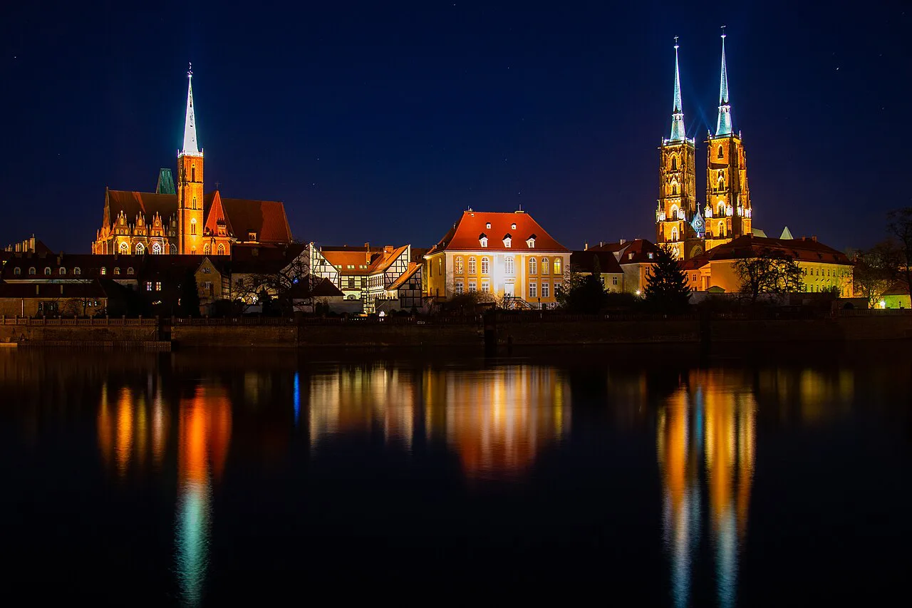 Ostrów Tumski in Wrocław lit up at night and reflected in the Oder.