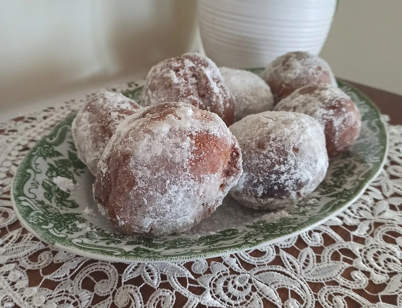 A plate of pączki dusted with icing sugar.