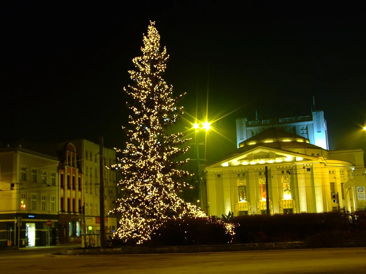 A Christmas tree on Katowice's Market Square in front of the illuminated Silesian Theatre.